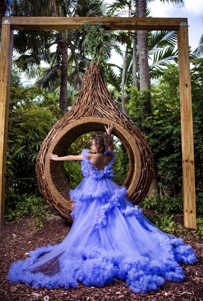 Villas photoshoot at Secret Gardens Miami showing a quinceañera in a blue ruffled gown on a woven wooden art structure.