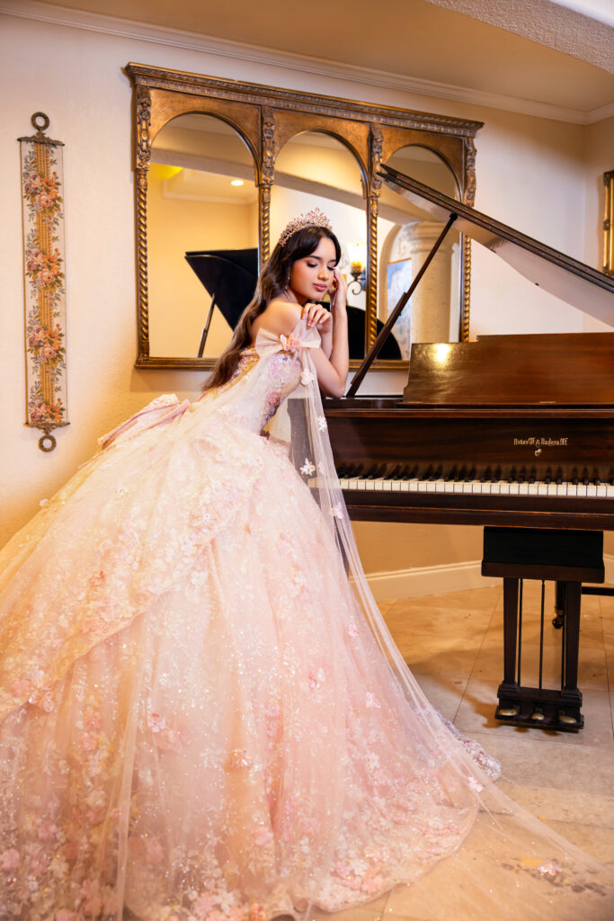 Villas photoshoot inside Villa Toscana Miami featuring a quinceañera in a blush ball gown posing beside a grand piano in an elegant interior.