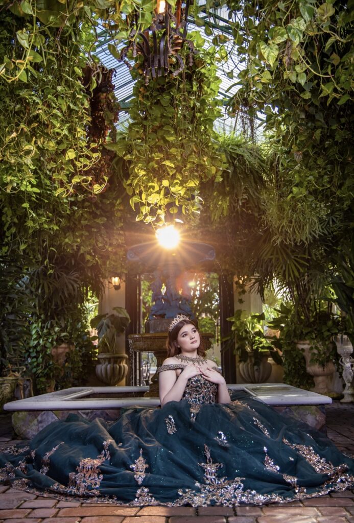 Villas photoshoot at Villa Toscana Miami with a quinceañera in an emerald dress surrounded by lush greenery and glowing sunlight.