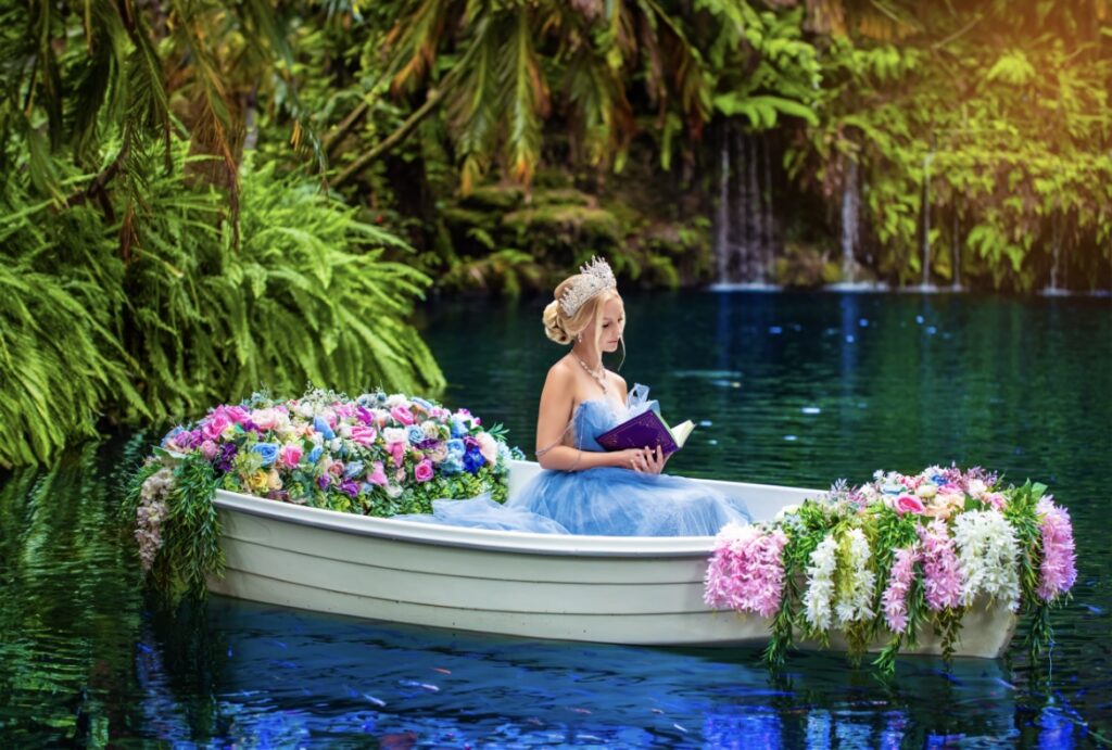 villas photoshoot at Villa Turquesa in Homestead FL – quinceañera in a blue gown sitting in a decorated white boat surrounded by vibrant flowers on turquoise water.