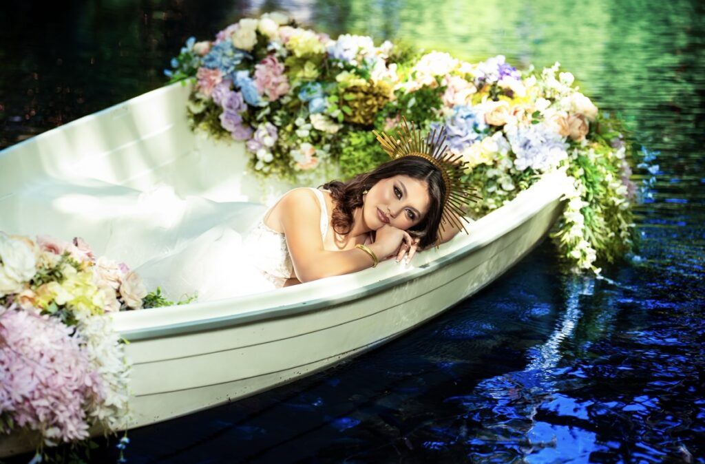 villas photoshoot at Villa Turquesa in Homestead FL – quinceañera lying in a flower-decorated boat floating on a serene blue lagoon.