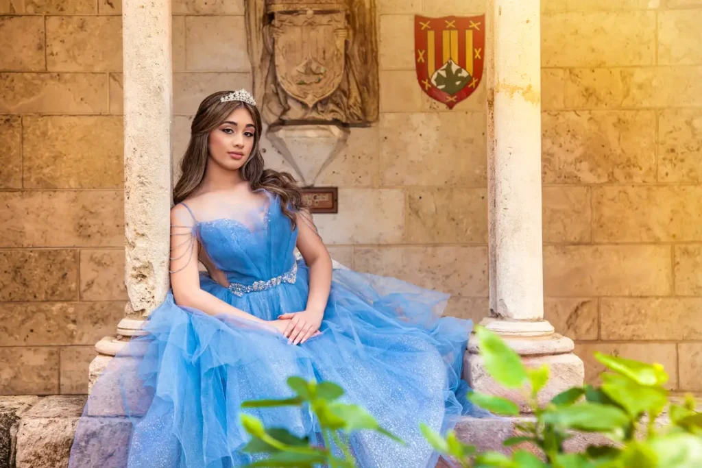 Castle quince photography at the Spanish Monastery: blue gown seated between stone columns with crest and warm sunset light.